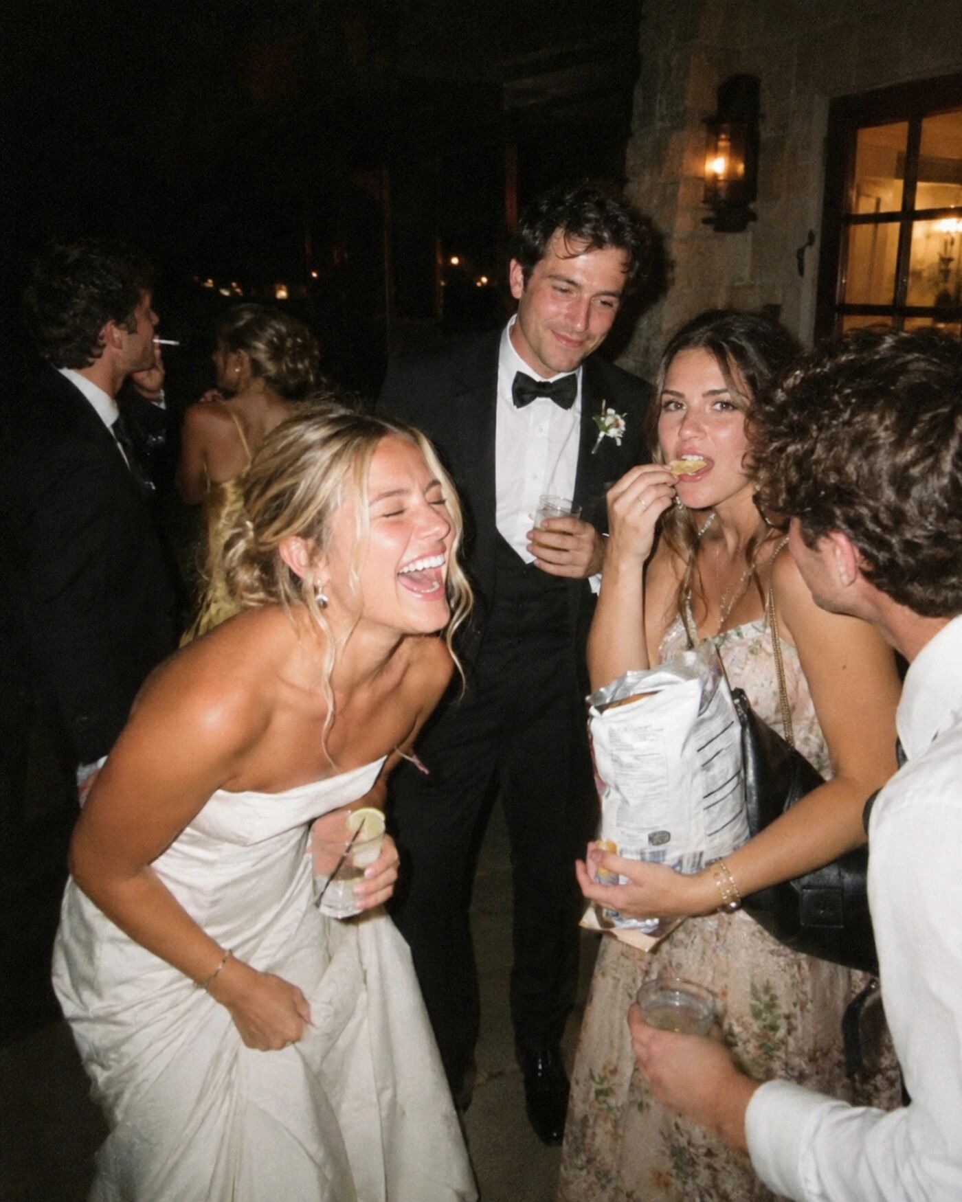 A bride laughing on the dancefloor, a guest with popcorn behind her