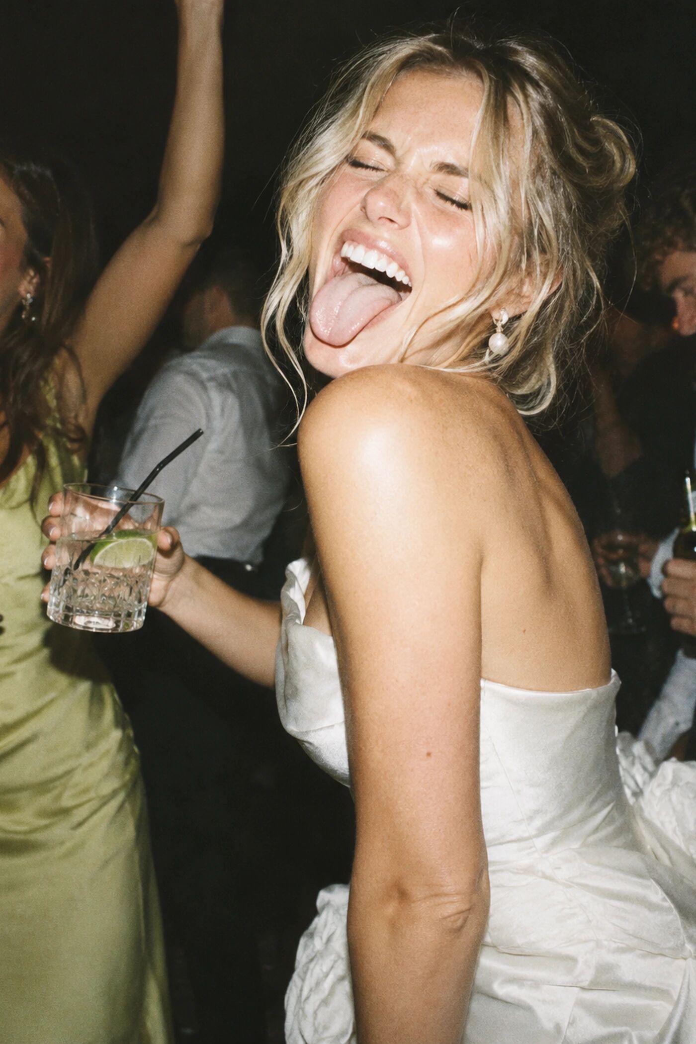 A bride laughing with her tongue out, bridesmaid behind