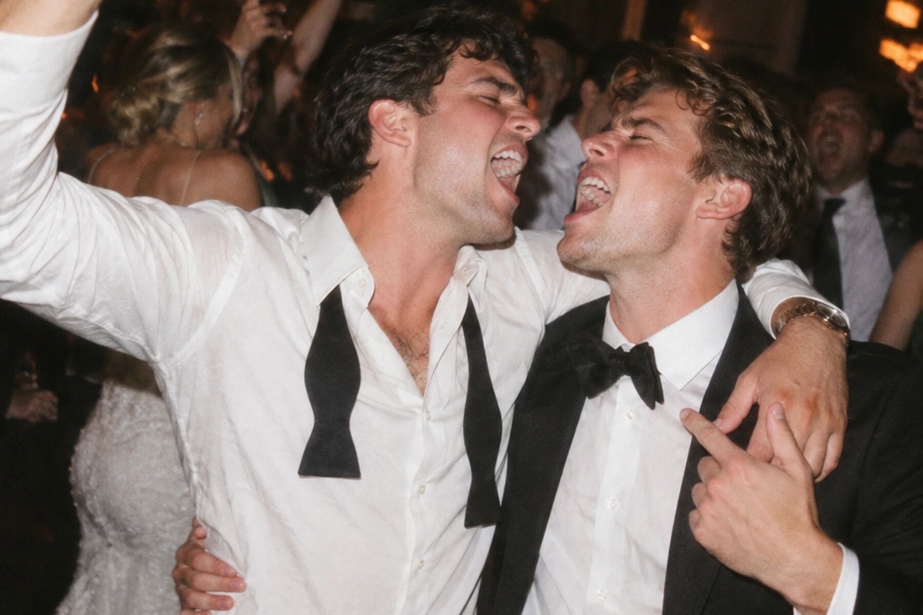 Two groomsmen shouting with joy, bow ties undone, direct flash