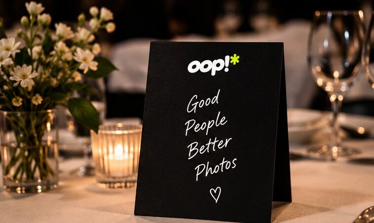 A black oop tent card reading “Good People Better Photos” on a dinner table with flowers and a candle
